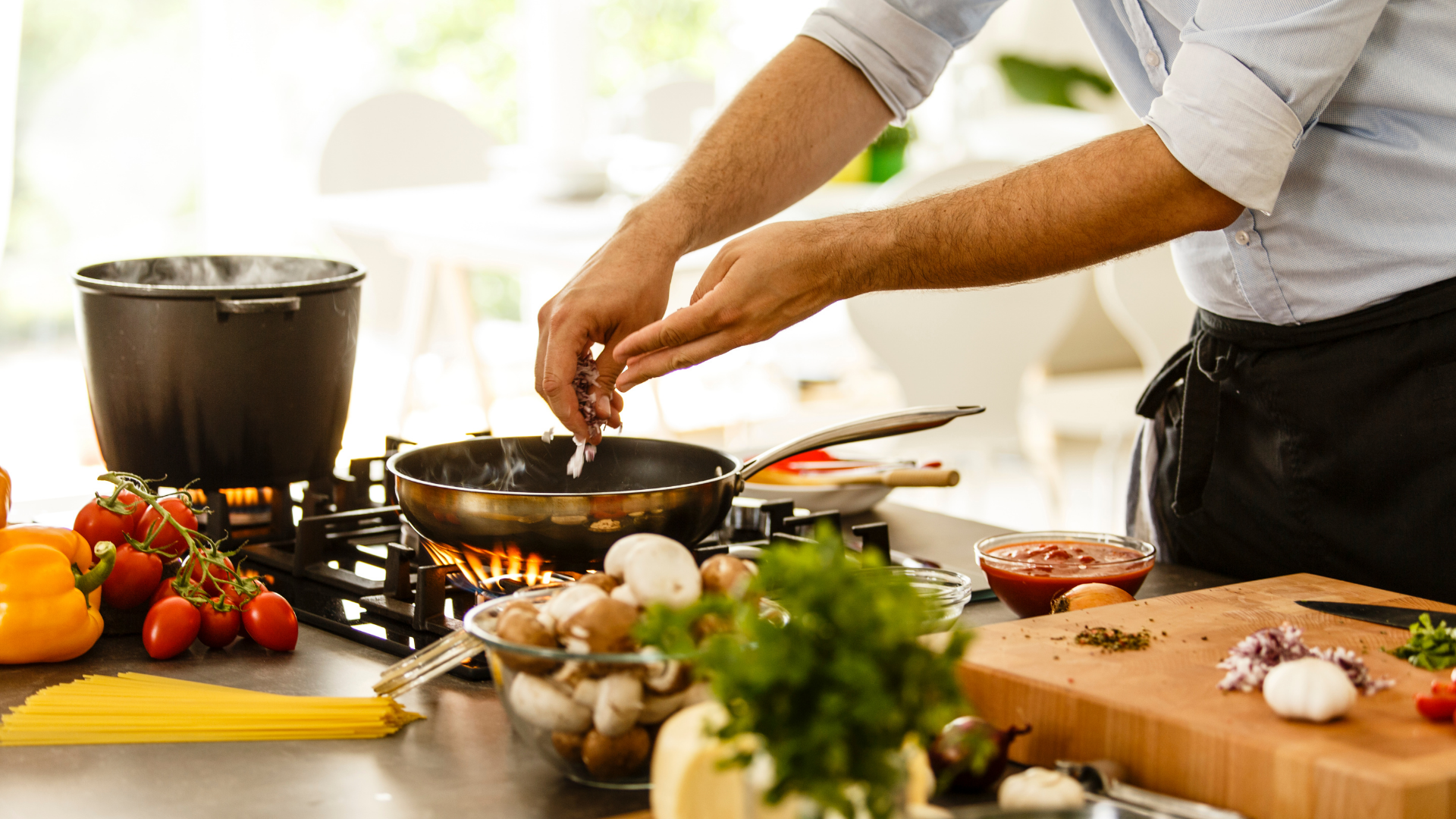 Chef seasoning a pan over a commercial kitchen flame